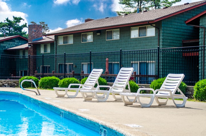 a group of lounge chairs next to a swimming pool in front of a house