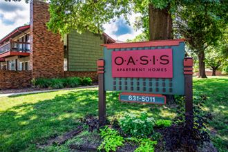 a sign for oasis apartment homes in front of a tree