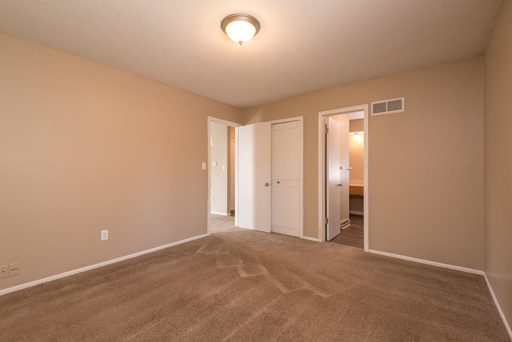 an empty living room with carpet and a door to a bedroom