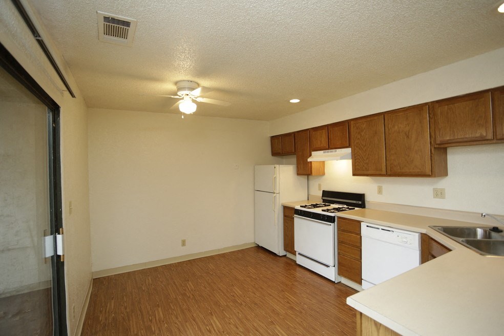 an empty kitchen with white appliances and wood flooring