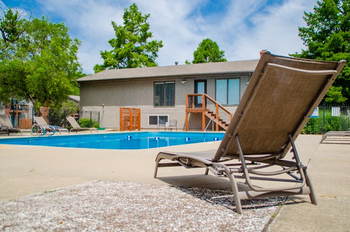a deck chair sits next to a pool in front of a house