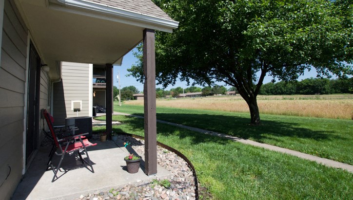 the front porch of a house with a lawn and a tree