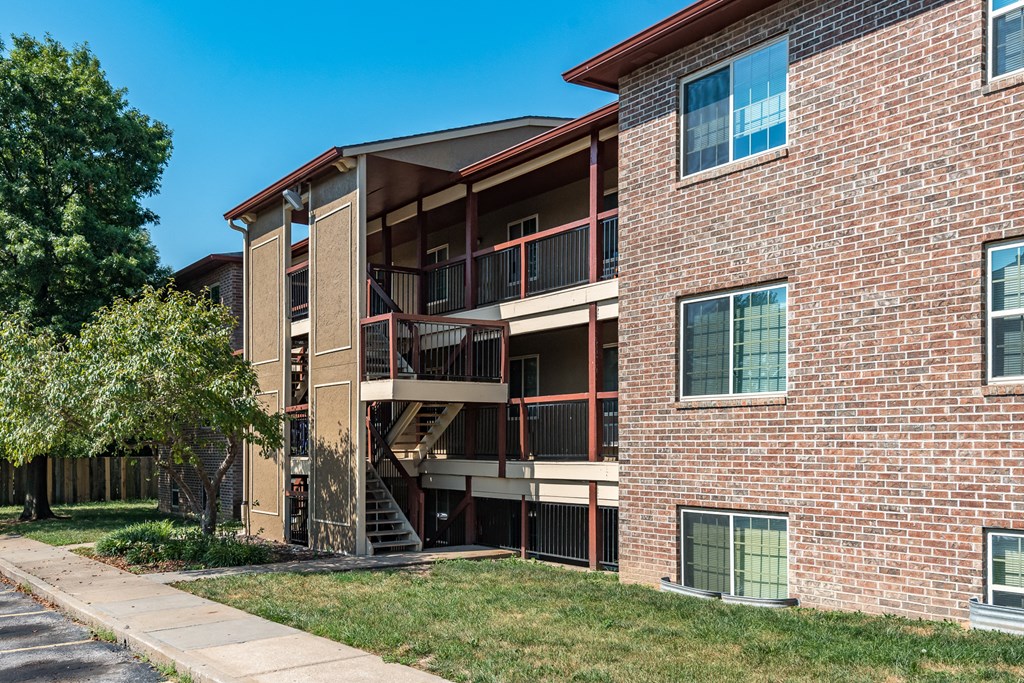 a brick apartment building with stairs and a tree in the yard