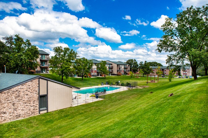 a swimming pool in the middle of a green field with apartments in the background