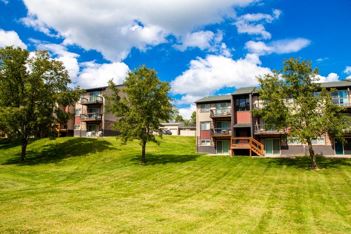 a row of apartment buildings on a grassy hill with trees