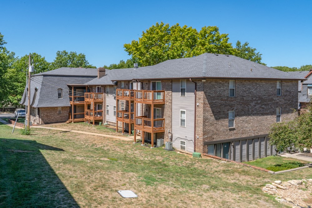 the back of a brick house with wooden balconies and a yard