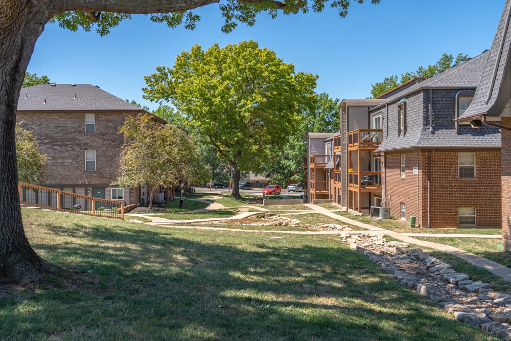 a view of the exterior of a brick apartment building with a yard and a tree