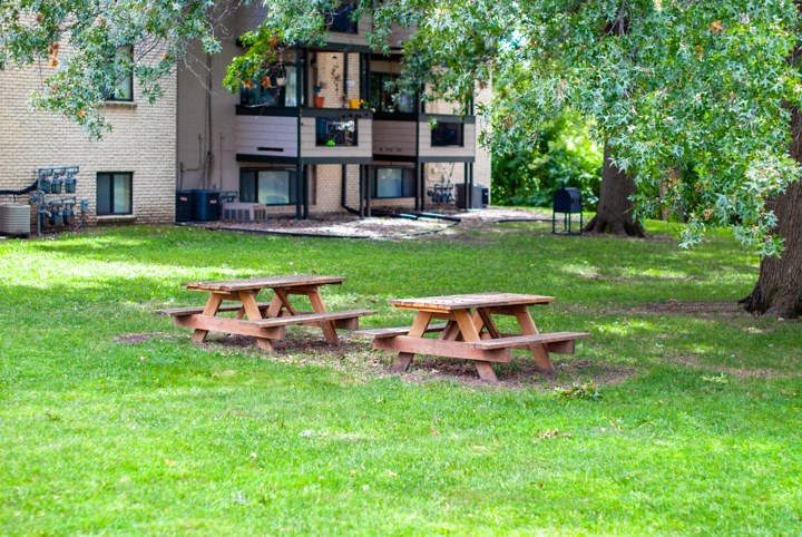 three picnic tables in a park in front of an apartment building