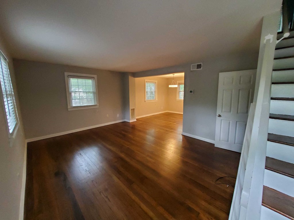 an empty living room with wooden floors and a white staircase