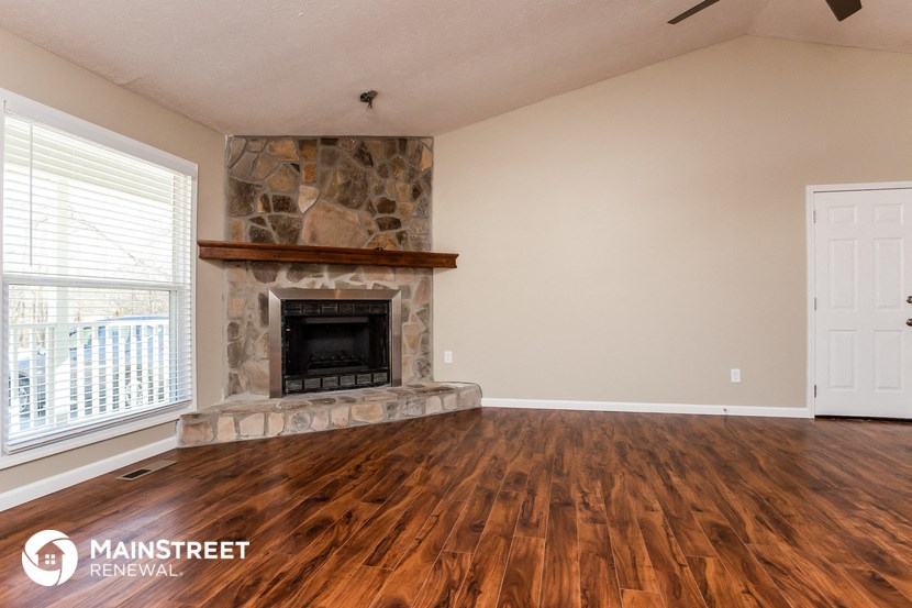 the living room with wood floors and a stone fireplace