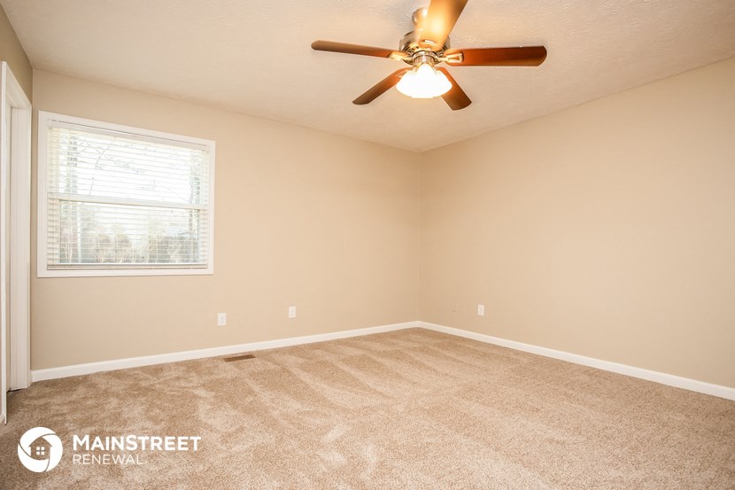 the spacious bedroom with carpeted flooring and a ceiling fan