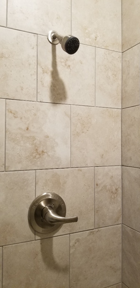 a shower handle in a tiled bathroom with a shadow on the wall