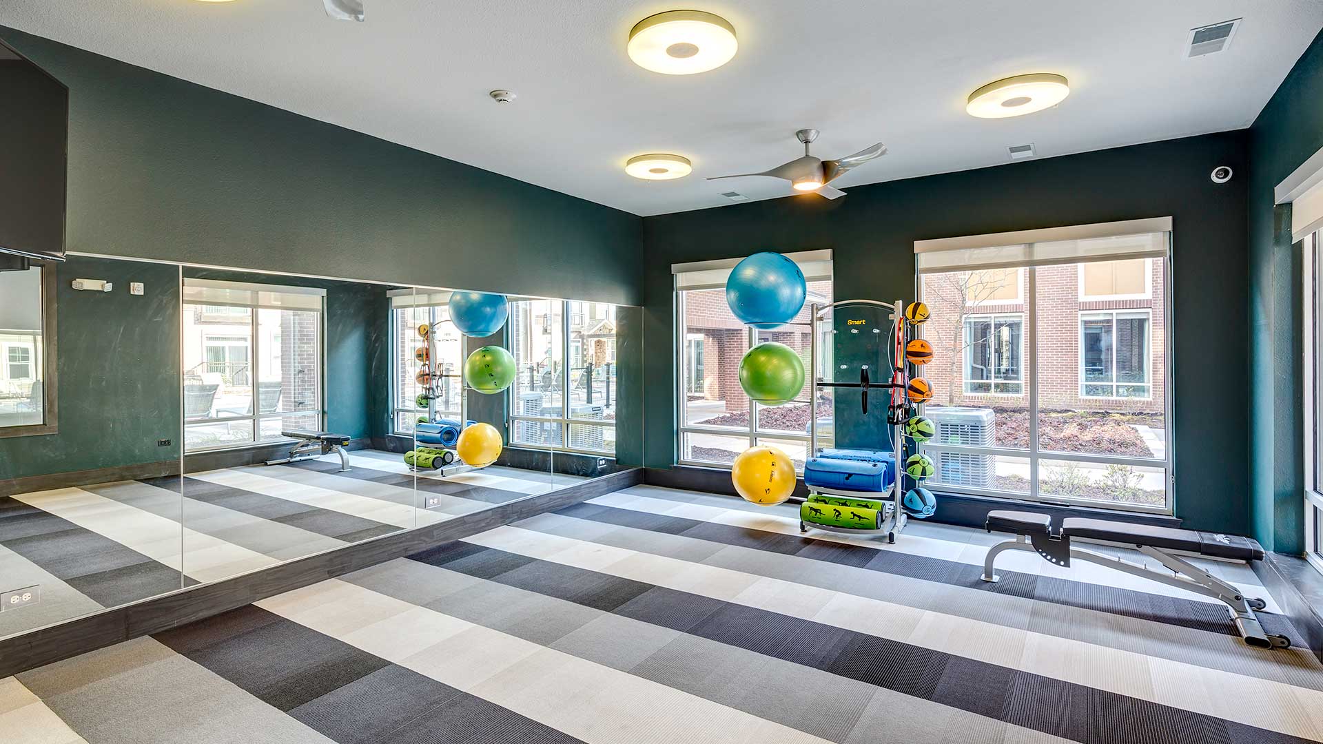 An open room with workout balls and a weight bench at the far end along the windows.
