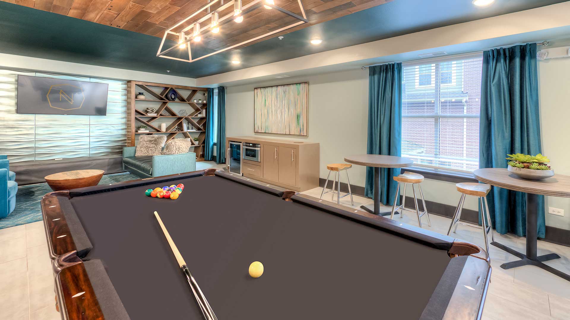 Looking across the brown felt of a pool table in the Game Lounge at Nort 680. There is seating all around the walls.