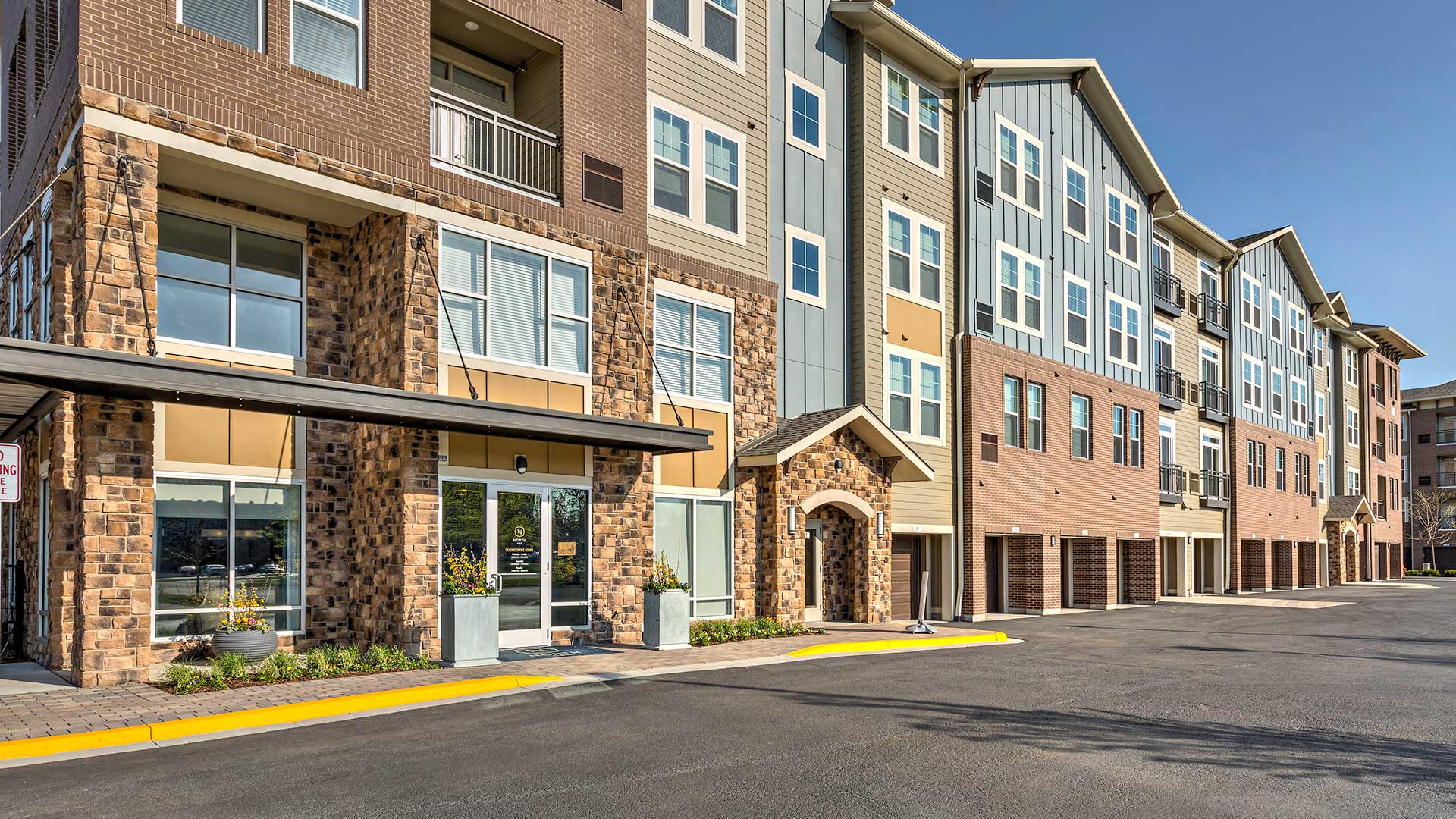 Looking along the front and front entrance to North 680. The office is on the left, and a row of garages is along the right. The building rises another three stories.