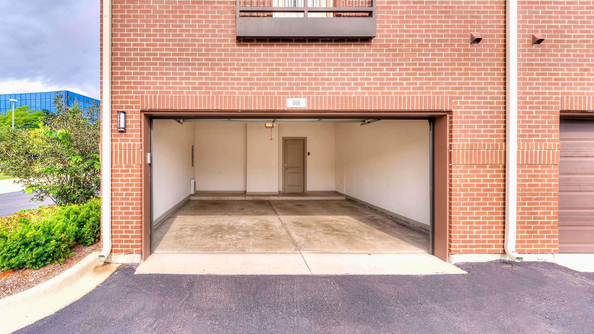 An empty two-car garage with a doorway into the residence at the back. The exterior of the building is red brick.