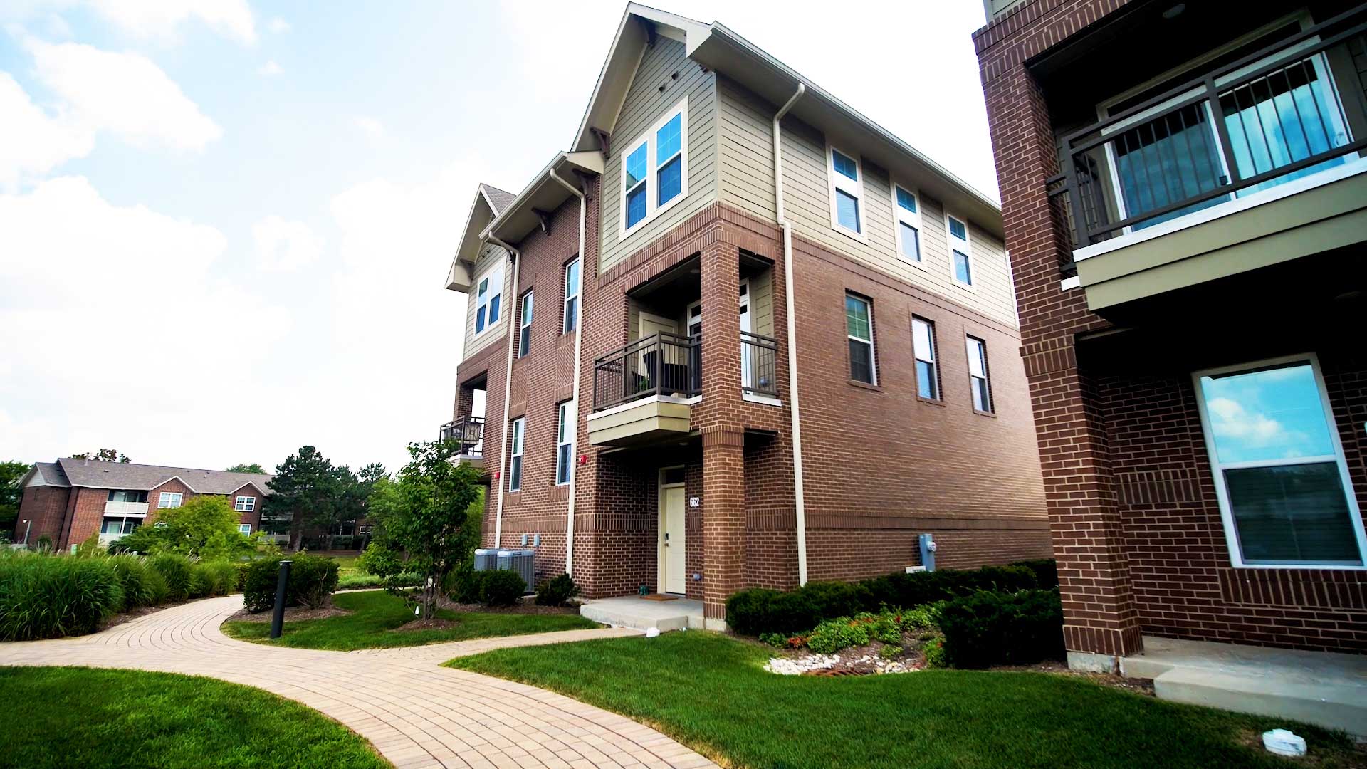 Looking up at one of the townhouses at North 680 from the brick walkway below. The building is mainly red brick with tan siding near the top. Green grass and shrubs fill the area.