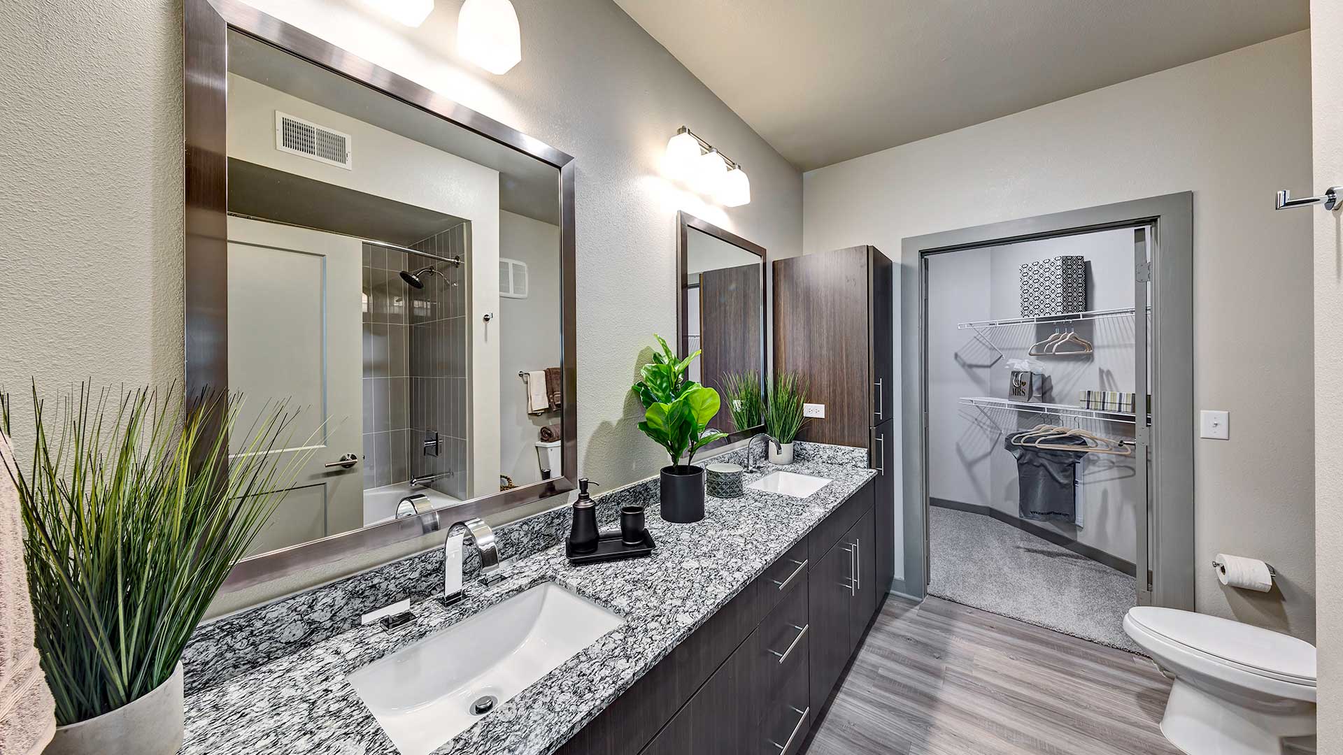 A double vanity runs along the left wall with a large cabinet at the end. The far wall has a large walk-in closet.