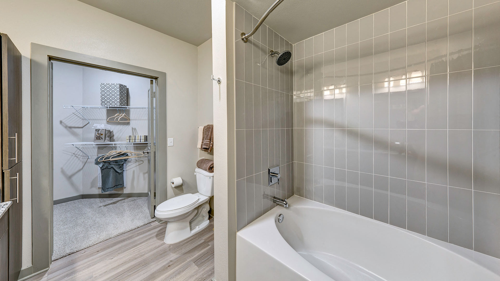 A large bathtub with grey tile is on the right. Off to the left is a toilet followed by a large walk-in closet.