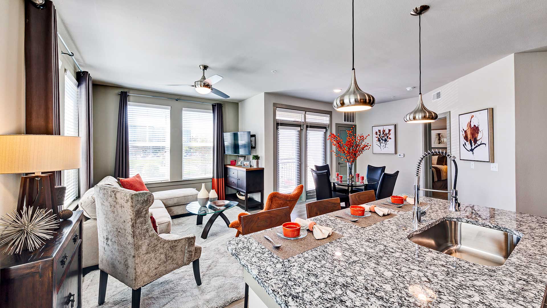 Looking across a kitchen island with a sink built-in at the living and dining room. The windows are open on a bright day. A doorway off to the right looks into the bedroom.