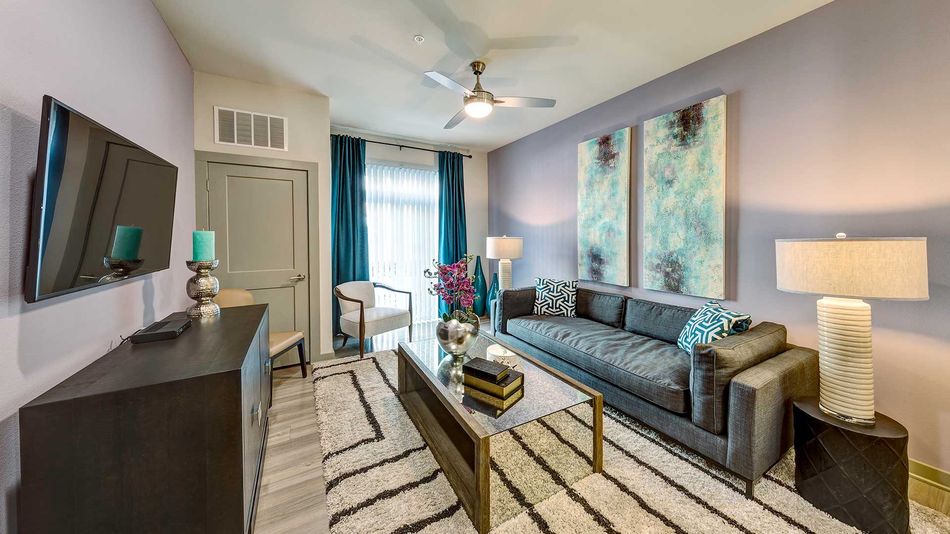 A living room at North 680. A couch sits against the far wall with an end table on either side and a coffee table in front. Across is a large cabinet and a wall-mounted television above.
