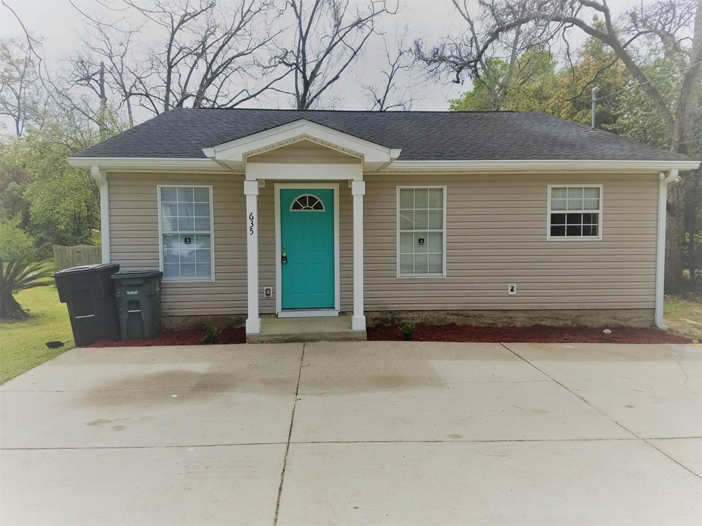 a small tan house with a green door and a driveway