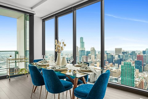 A dining room with blue chairs and a table set for a meal with a city view.