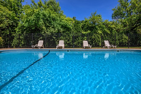 a swimming pool with chairs and trees in the background
