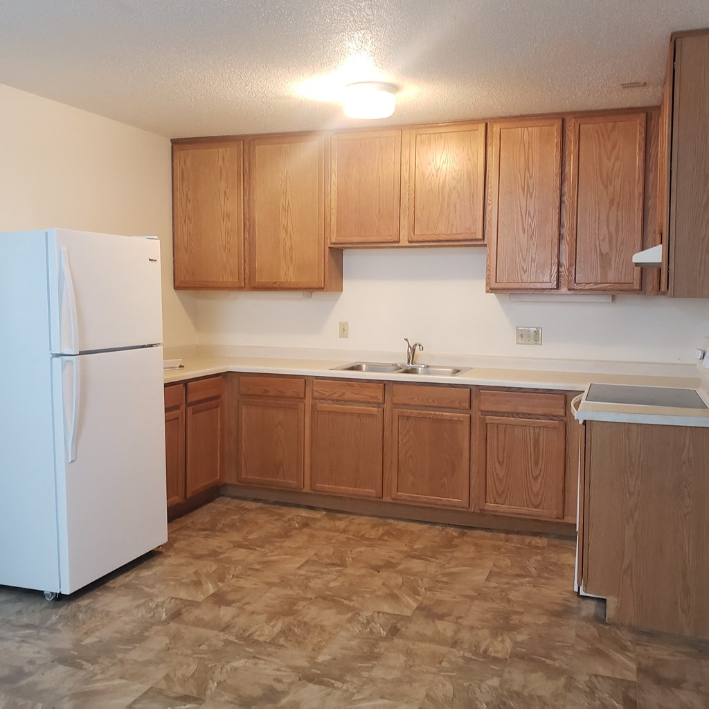 an empty kitchen with wooden cabinets and a refrigerator