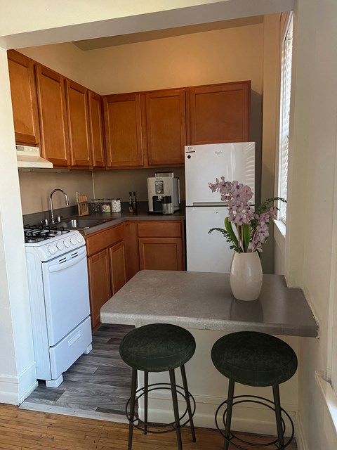 a kitchen with white appliances and wooden cabinets and a counter with two stools