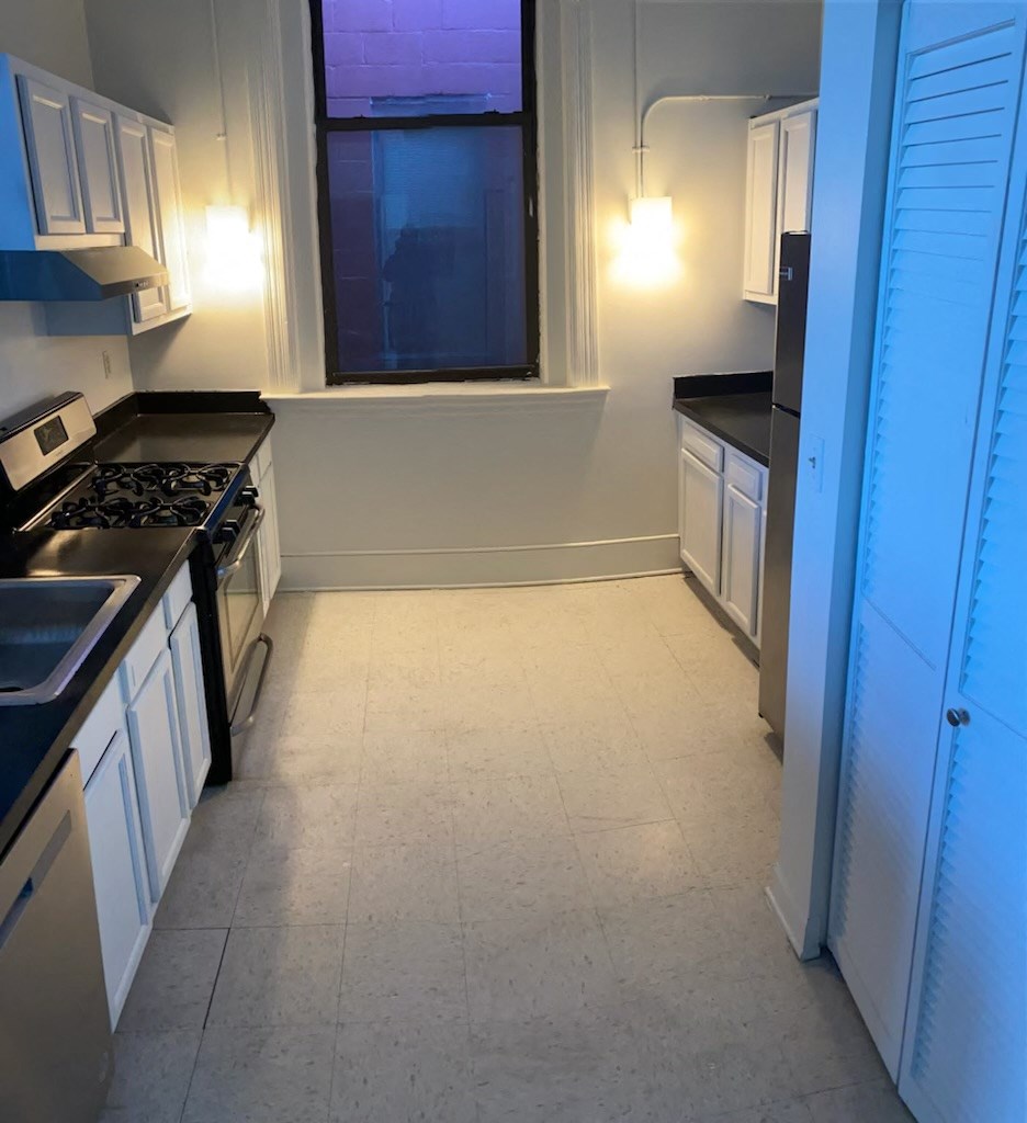 an empty kitchen with white cabinets and a window