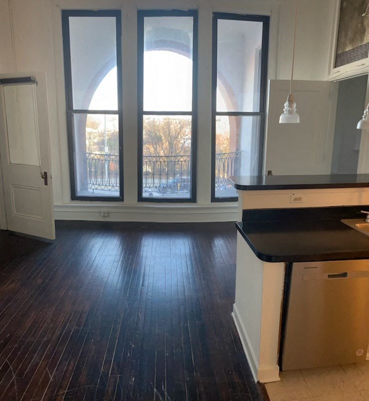 an empty living room with windows and a kitchen
