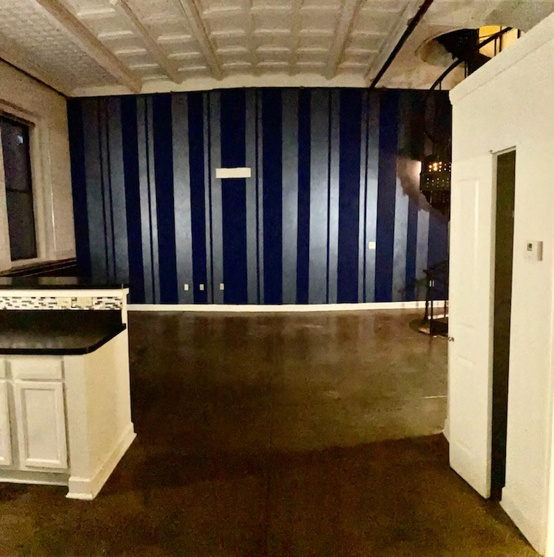 an empty living room with blue striped walls and a kitchen