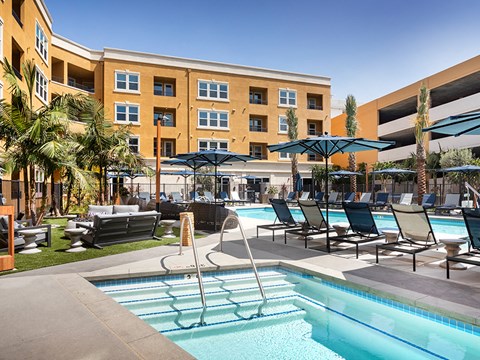 A pool area with lounge chairs and umbrellas in front of a multi-story building.