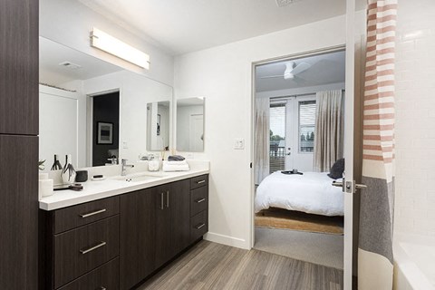 A bedroom with a large mirror, a vanity with a sink, and a bed with a white comforter.