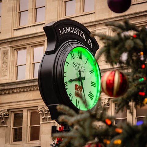 a clock on the side of a building next to a christmas tree