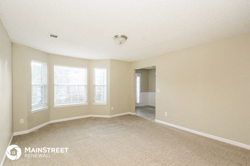 an empty living room with three windows and a carpet