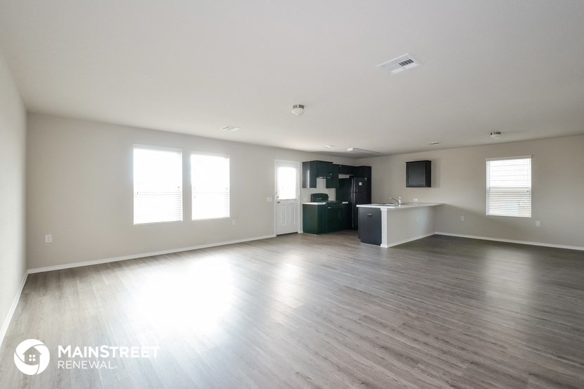 an empty living room with wood floors and a kitchen