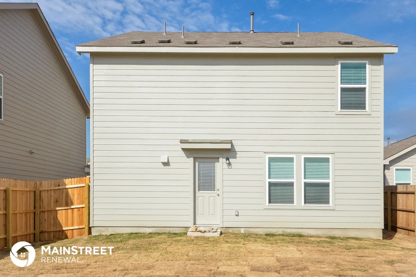 the backyard of a white house with a wooden fence