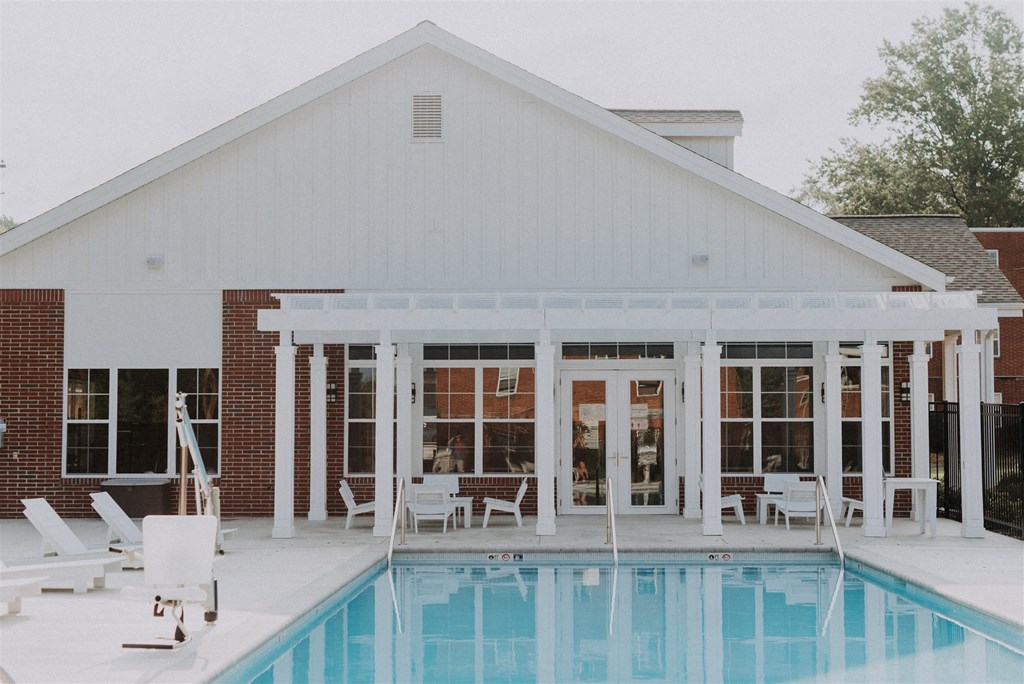 the pool and porch of a white house with white chairs and a swimming pool
