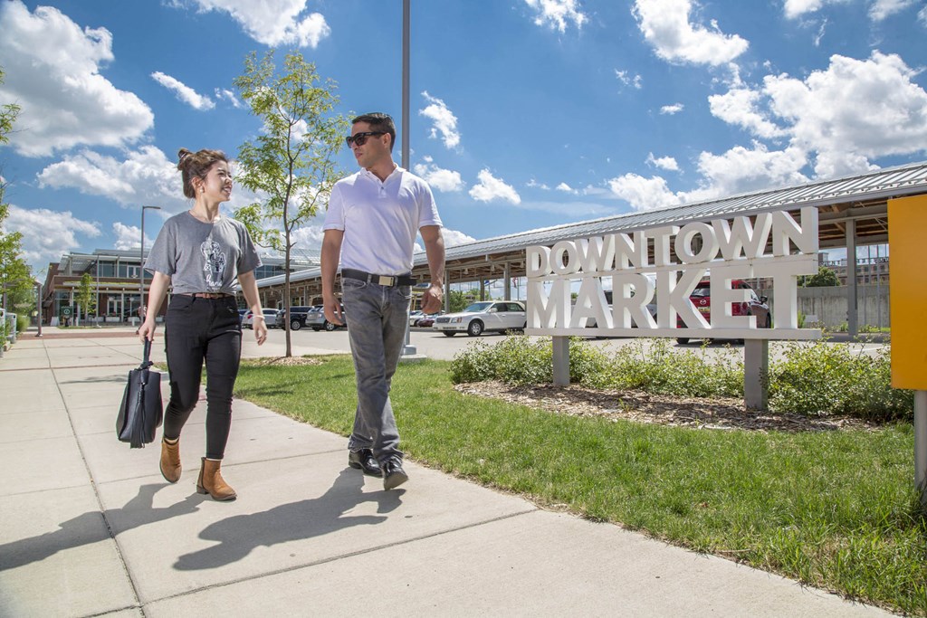 two men walking on a sidewalk in front of a downtown market sign