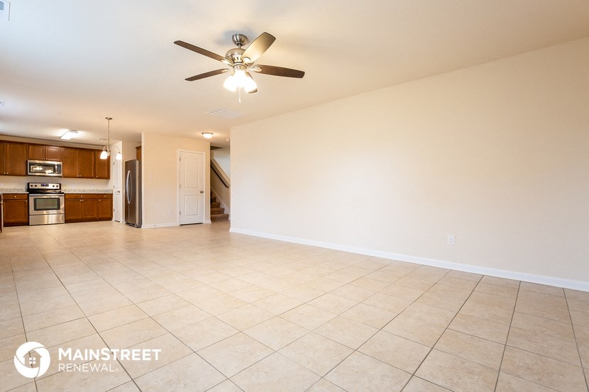an empty living room with a ceiling fan and a kitchen