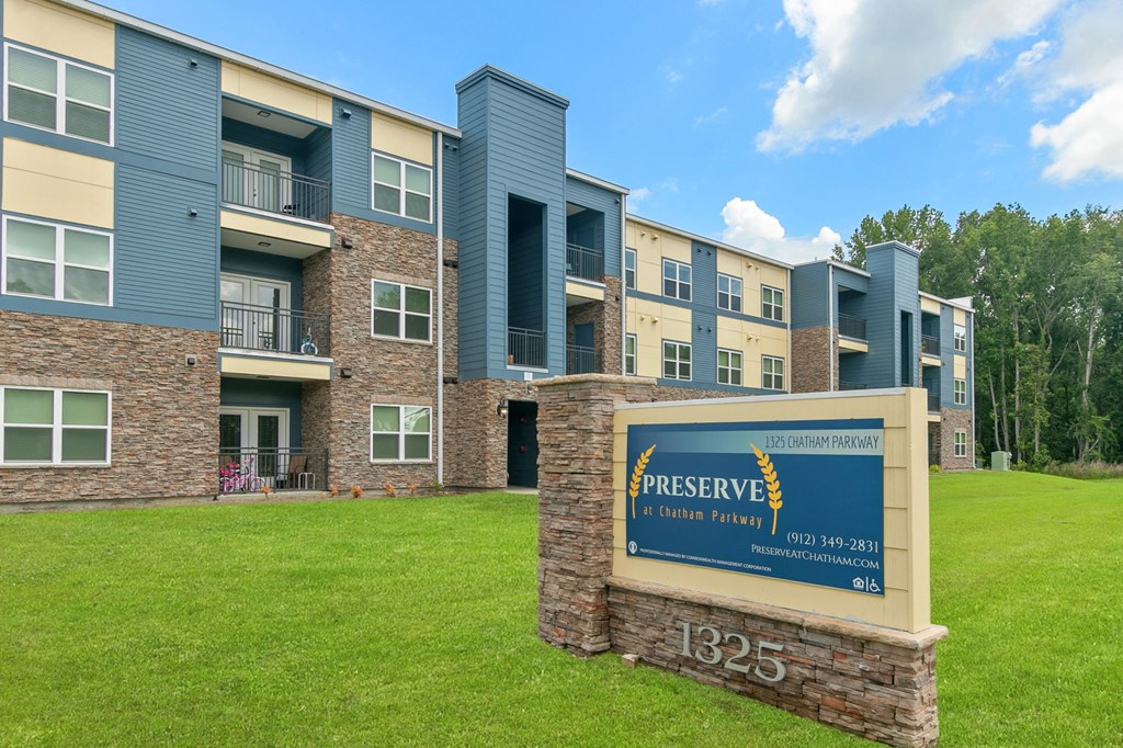 an apartment building with a green lawn and a sign in front of it