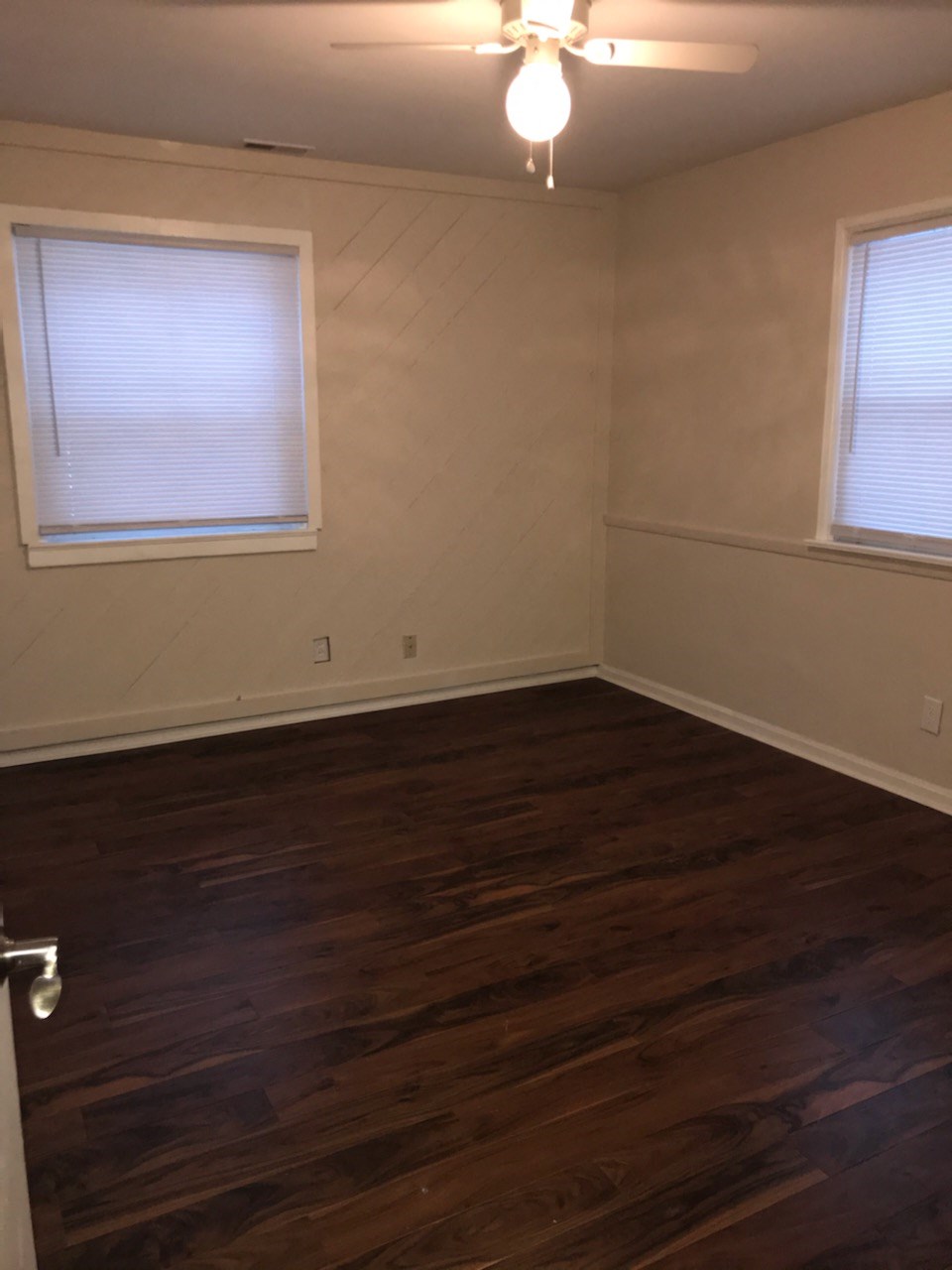an empty room with wooden floors and two windows