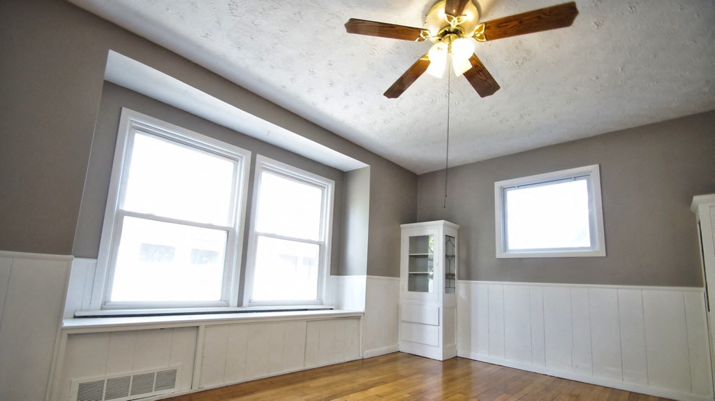 an empty living room with a ceiling fan and three windows