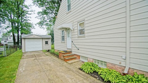 A house with a white siding and a small front yard with a concrete walkway.