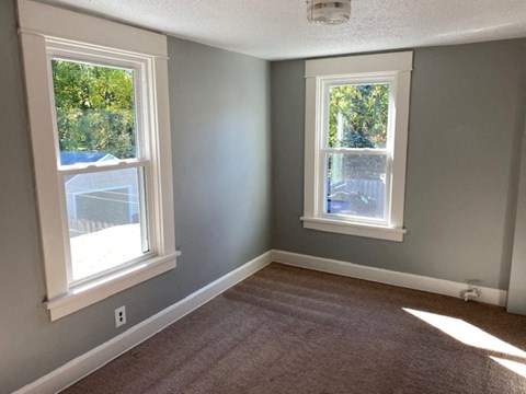 an empty room with two windows and a carpet
