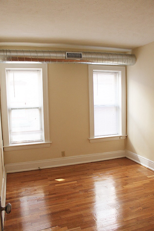 an empty room with a wood floor and two windows