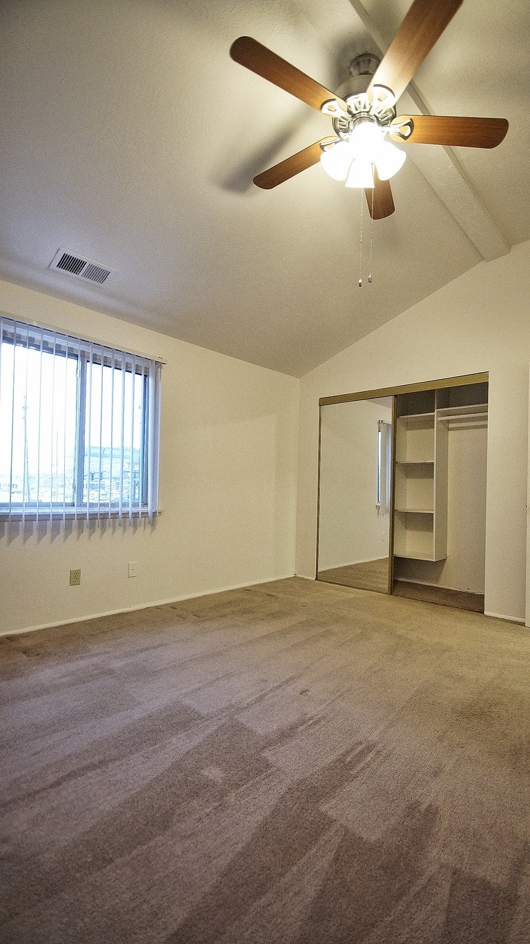 an empty living room with a ceiling fan and a closet