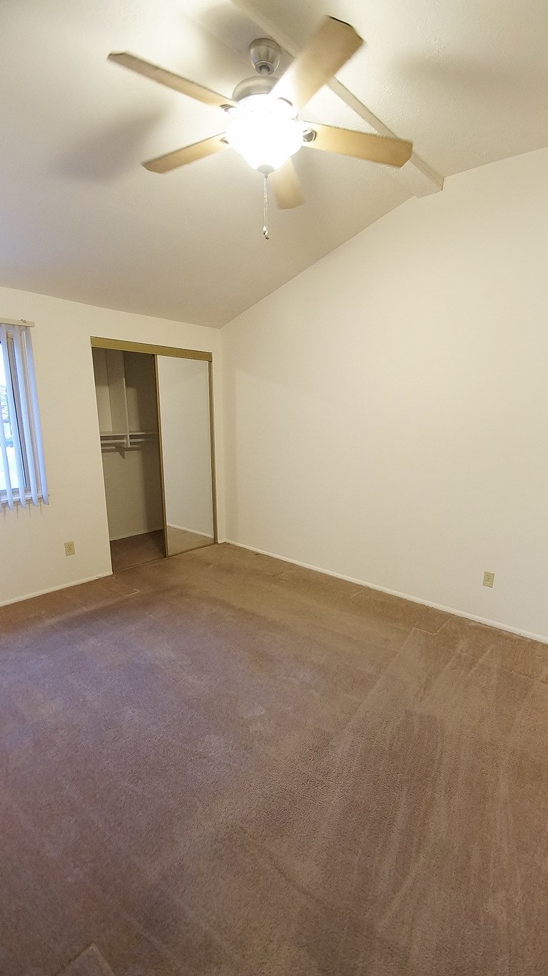 an empty living room with a ceiling fan and a closet